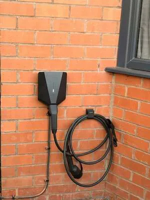 Smart EV charger with tethered cable mounted on a red brick wall beside a window