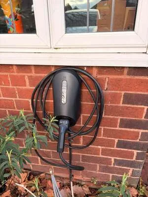 Black EV charger with coiled charging cable fitted below a window