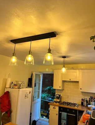 Three glass pendant lights on a bar fitting above a kitchen worktop