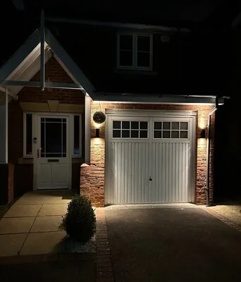 Porch and garage frontage lit at night by wall lights
