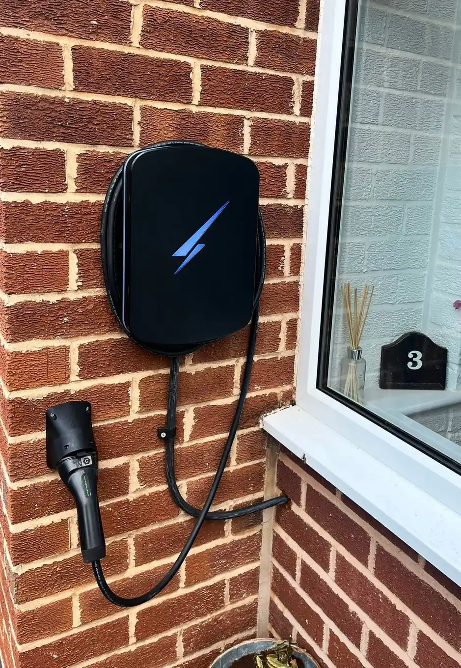 Black smart EV charger fitted on a red brick wall