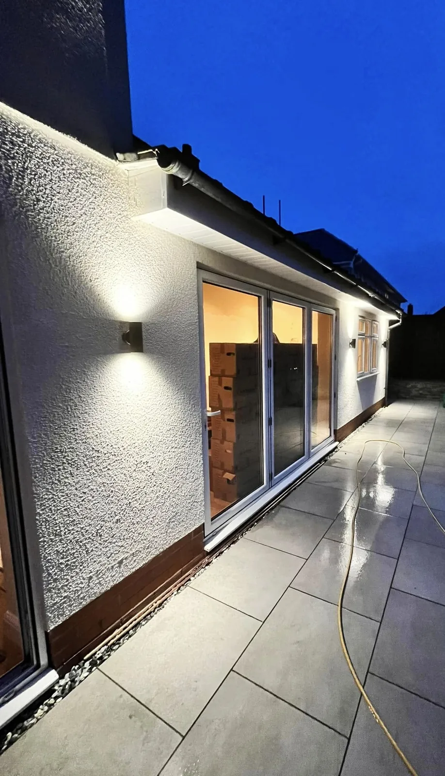 Outdoor wall lights along a rendered extension at dusk